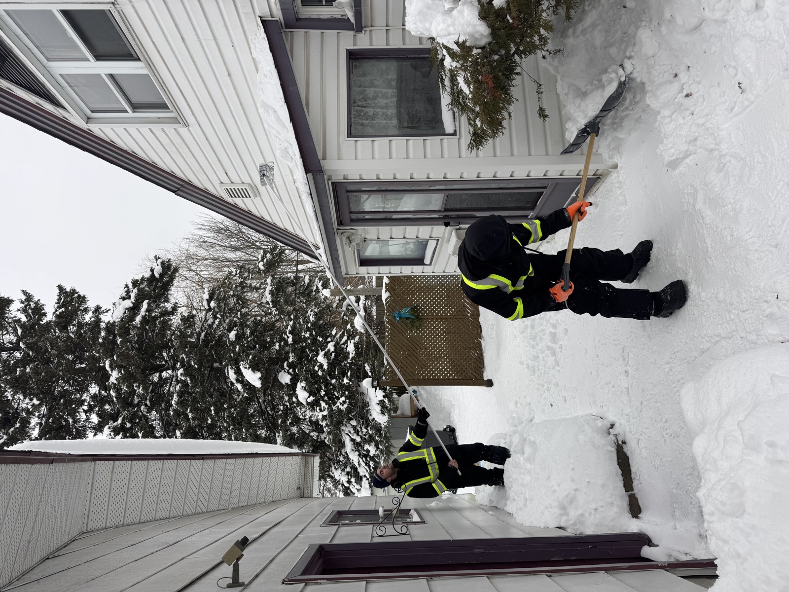 Two Roofline crew members clearing snow together between two buildings